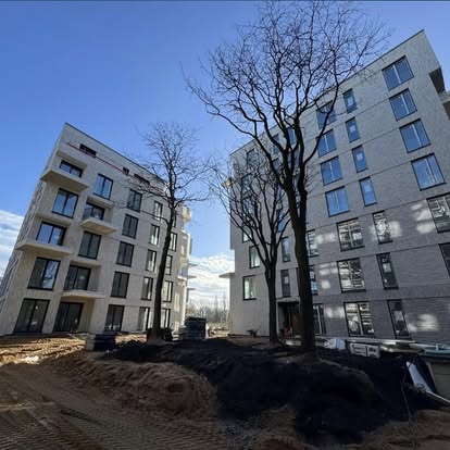 Zwei moderne Wohngebäude mit großen Fenstern und Bäumen im Hintergrund.