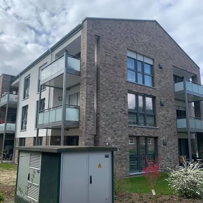 Moderne Wohnanlage mit Steinfassade und Balkonen, umgeben von Grünflächen mit neuen Klinkerriemchen 