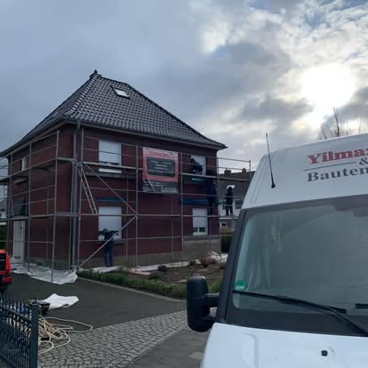 Renoviertes Haus mit Gerüst, Bauwagen und wolkigem Himmel.