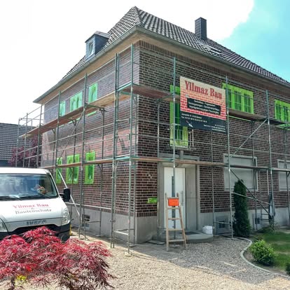 Renoviertes Haus mit Gerüst und Bauwagen und einem kleinen Garten.
