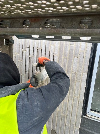 Arbeiter in gelber Weste schneidet Fliesen mit Werkzeug an einer Wand.