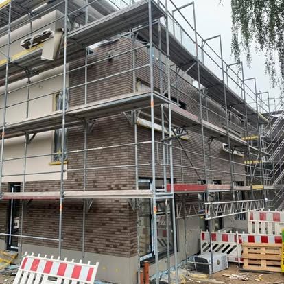 Baustelle mit Gerüst und Mauerwerk im Bau, umgeben von Absperrungen.