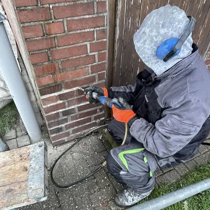 Handwerker mit gelbem Helm entfernt alte Fugen